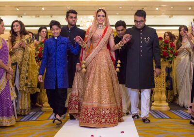 Bride walking down aisle with family during Hindu wedding celebration.