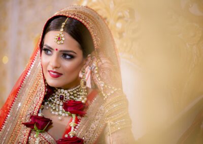 Bride in red lehenga with gold jewellery and rose garland.