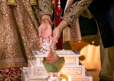 Bride and groom performing Hindu ritual by offering rice into sacred fire.