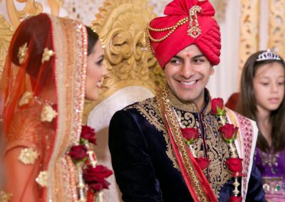 Groom smiling at bride during Hindu wedding ceremony with floral garlands.
