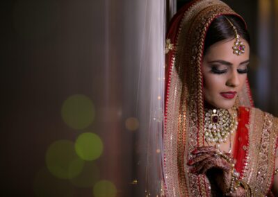 Bride in red bridal attire with jewellery and mehndi posing before ceremony.