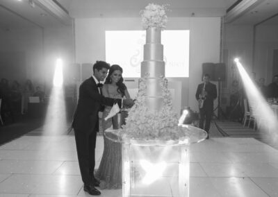 Black-and-white shot of couple cutting elegant multi-tiered wedding cake.