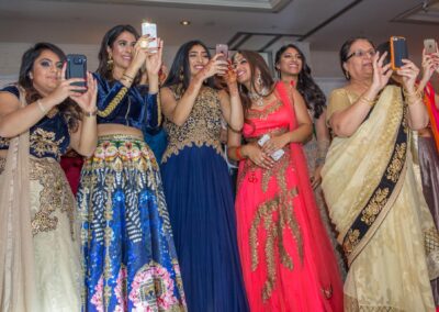 Guests in colourful sarees and lehengas capturing wedding moments on their phones.