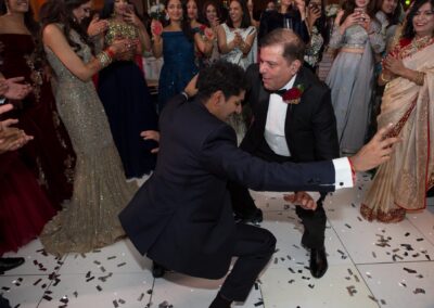 Groom and father dancing surrounded by guests during wedding celebration.