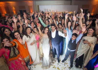 Bride and groom celebrating with guests raising hands during wedding reception.