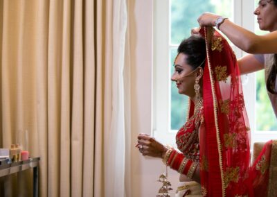 Makeup artist adjusting bride’s red embroidered dupatta before Hindu wedding ceremony.