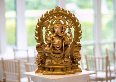 Golden Lord Ganesha idol placed on white pedestal at Hindu wedding ceremony venue.