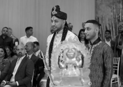 Groom standing with groomsman holding sword during traditional Hindu wedding ceremony.