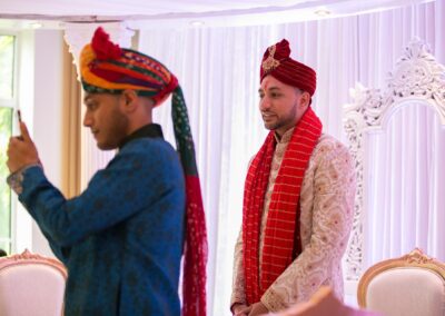 Groom smiling while guest photographs him during wedding ceremony.