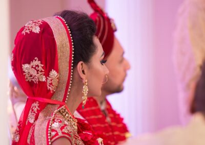 Bride in red dupatta and groom in turban seated during Hindu wedding ceremony.