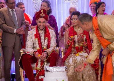 Bride and groom smiling during Hindu wedding ritual with guests gathered around.