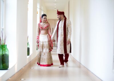 Bride and groom walking hand in hand through bright hallway in elegant wedding attire.