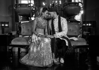 Bride and groom sitting closely on vintage sofa, captured in black and white portrait.