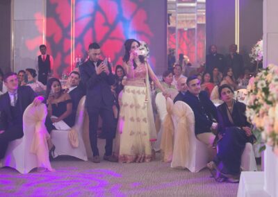 Guests watching wedding speeches while bride records moment on phone.