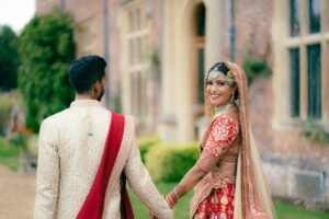 A bride looking back and smiling while holding the groom's hand outdoors.
