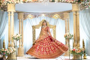 A bride in a red and gold gown twirls elegantly on a decorated stage.