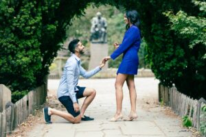 A man proposes to a woman on a pathway lined with hedges.