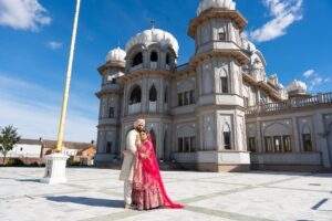 A bride and groom pose in front of a grand, ornate temple building.