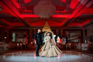 A bride and groom dancing on a stage under a chandelier with red lighting.