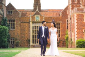 A bride and groom walk hand-in-hand in front of a historic building.