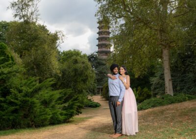 Couple embracing outdoors with tall pagoda visible in lush green garden background.