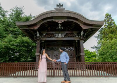 Couple holding hands in front of traditional Japanese-style wooden pavilion.