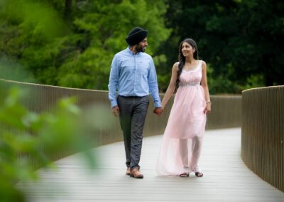 Couple walking hand in hand on bridge surrounded by lush green trees.