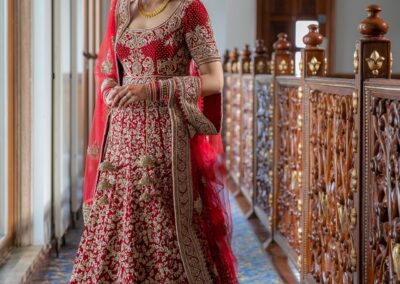 Sikh bride in red embroidered lehenga standing gracefully inside Gurdwara hallway.