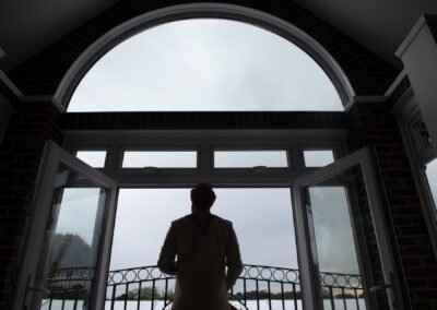 Silhouette of Sikh groom standing near arched window before wedding ceremony preparation.
