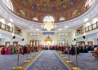 Wide interior view of decorated Gurdwara hall during Sikh wedding ceremony.