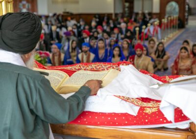 Sikh priest reading Guru Granth Sahib as wedding guests listen during ceremony.