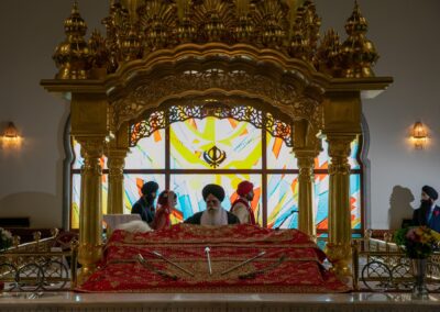 Sikh priest performing rituals as couple stands before sacred scripture at Gurdwara.