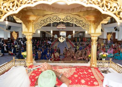 Wedding guests seated in Gurdwara during religious ceremony under golden canopy.