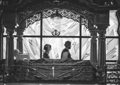 Bride and groom walking in Gurdwara during Sikh wedding ceremony with sacred backdrop.