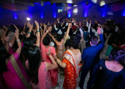 Wedding guests dancing with raised hands at colourful reception celebration.