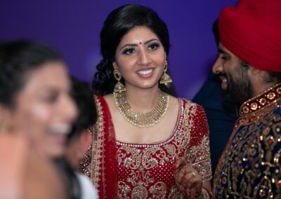 Bride smiling in red bridal lehenga adorned with gold jewellery during reception.