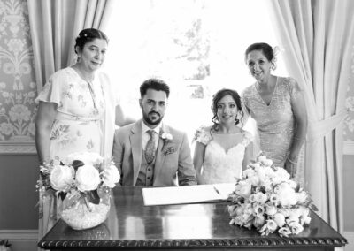 Bride and groom sitting at signing table with family members after ceremony.