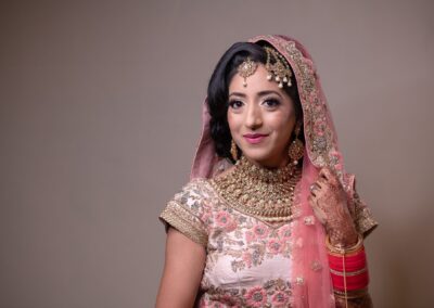 Bride in pink lehenga smiling with jewellery and mehndi before wedding ceremony.