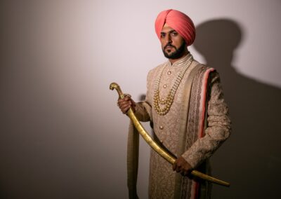 Sikh groom in ornate sherwani and turban holding golden curved sword.
