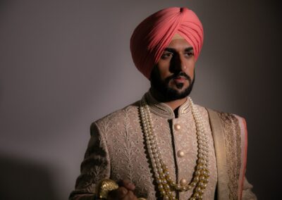 Sikh groom in beige sherwani and pearl necklace posing before wedding.