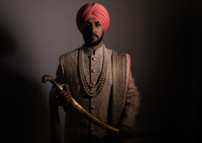 Sikh groom in peach turban holding golden sword in traditional wedding attire.